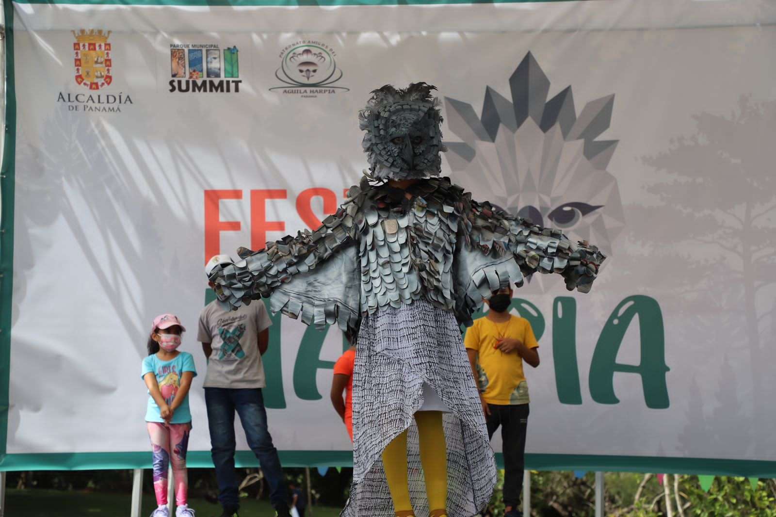 En la foto se puede ver una persona disfrazada de aguila harpia junto a unos niños en la tarima del festi harpia 2022